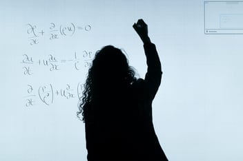 A woman is writing equations on a whiteboard